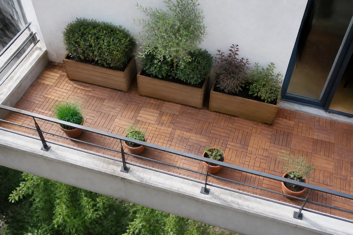 Balcon étroit d’immeuble avec bacs répartis le long du mur porteur et pots plus légers en bordure
